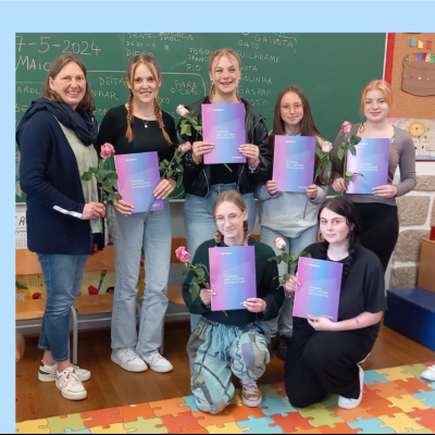 Auf dem Bild sind Schülerinnen zu sehen die ein Blatt Papier vor sich halten.